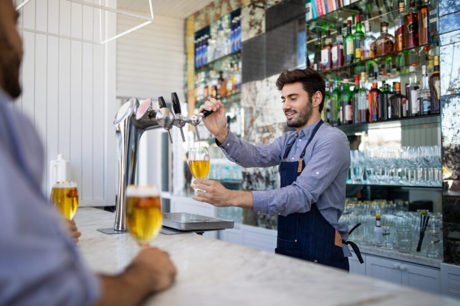 Bartender pouring beer in a glass. Barman filling a beer in a glass from the tap with customer sitting at the counter.