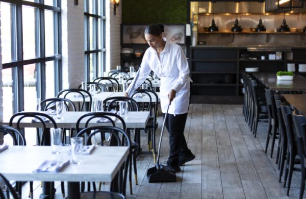 A worker sweeping the floor in an empty restaurant. The mid adult woman in her 30s is mixed race African-American, Native American and Caucasian. She is looking down at the floor with a serious expression.