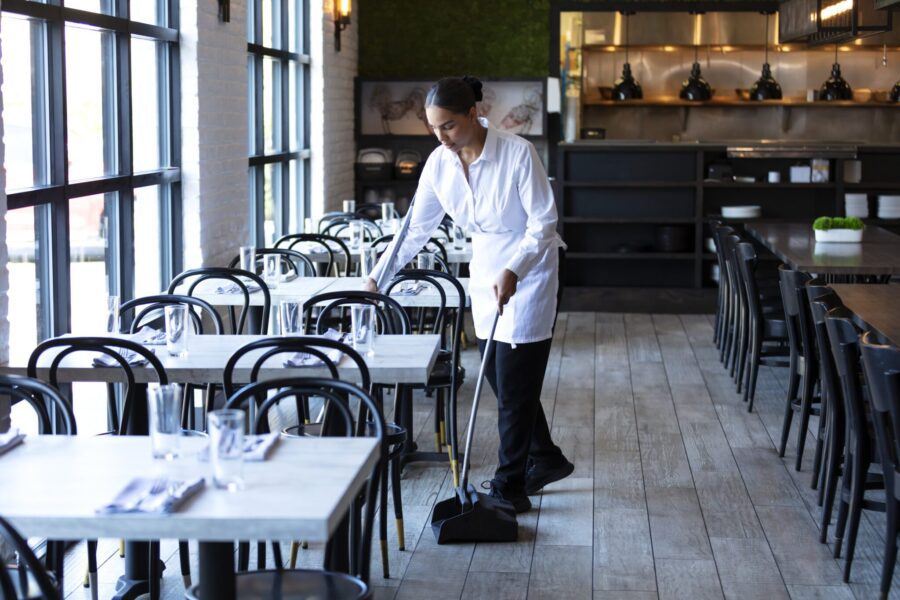 A worker sweeping the floor in an empty restaurant. The mid adult woman in her 30s is mixed race African-American, Native American and Caucasian. She is looking down at the floor with a serious expression.