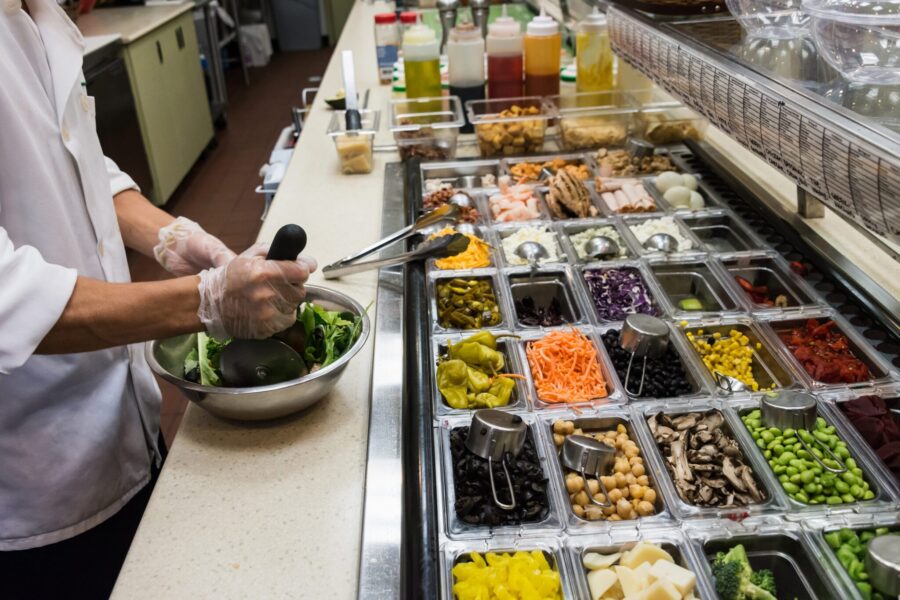 Close up picture of a chef preparing a stainless steel bowl full of assorted salad with salad ingredients