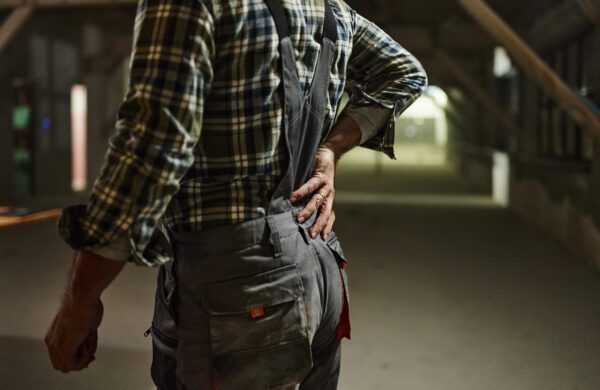 Unrecognizable manual worker holding his back in pain at construction site