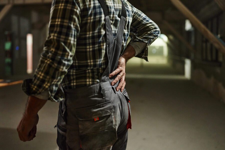 Unrecognizable manual worker holding his back in pain at construction site