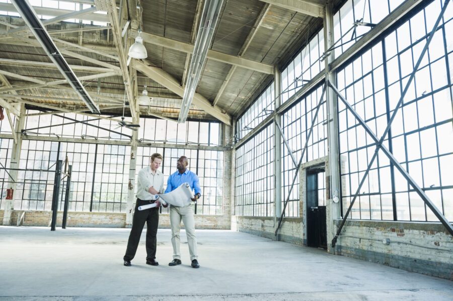 Businessmen reading blueprints in empty warehouse