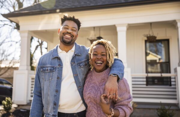 Portrait of husband and wife embracing in front of home