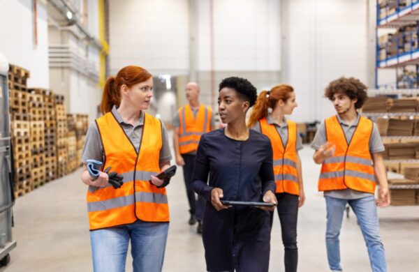 Warehouse manager discussing delivery schedules with a female worker. Warehouse supervisor walking and talking with dispatch worker.