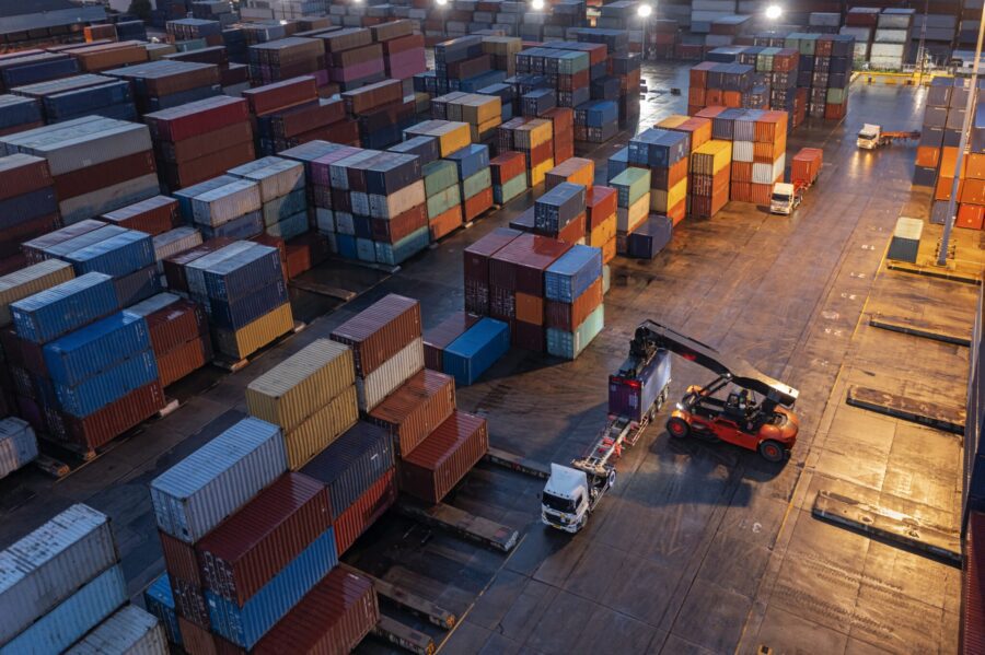 Aerial view forklift handling container load to container truck at night for business logistics, import export, shipping or freight transportation.