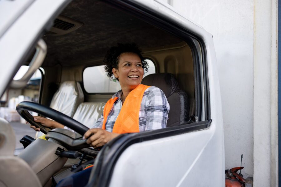 Happy Latin American female truck driver smiling while driving her vehicle - freight transportation concepts
