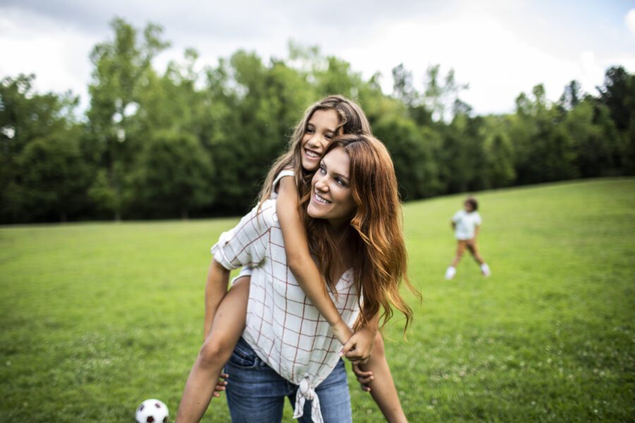 Daughter riding on mothers shoulders at park