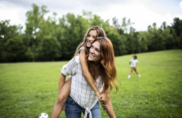 Daughter riding on mothers shoulders at park
