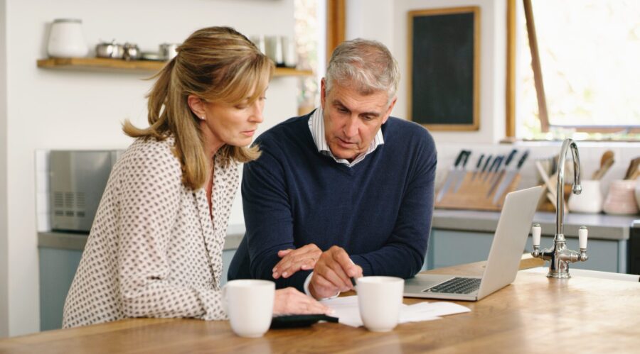 A senior couple planning their finance and paying bills while using a laptop at home. A mature man and woman going through paperwork and working online with a computer