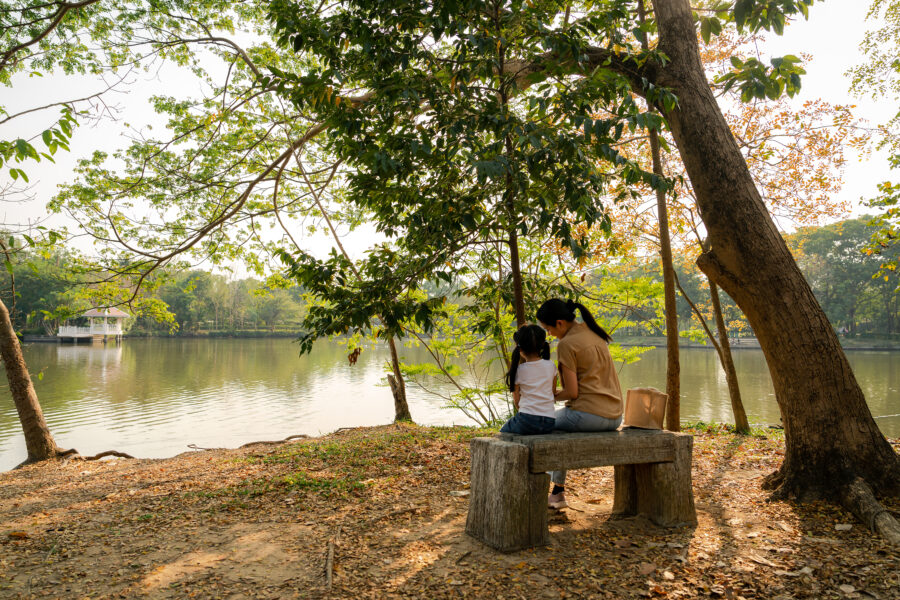 Asian mother sitting with daughter at lake in the park