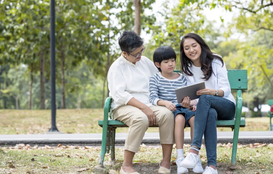 Multi Asian family spending time in weekend holiday. Young mother and grandmother teaching grandson using digital tablet to searching knowledge from internet.