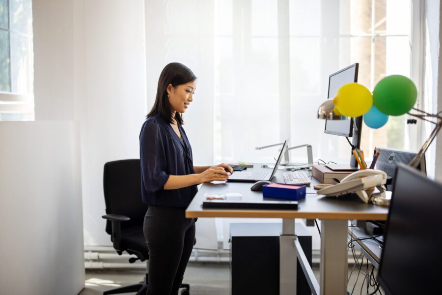 Female having a video call on her laptop in office. Woman working at ergonomic standing desk having a teleconference.