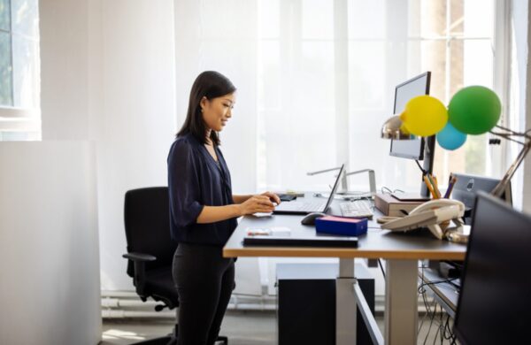 Female having a video call on her laptop in office. Woman working at ergonomic standing desk having a teleconference.
