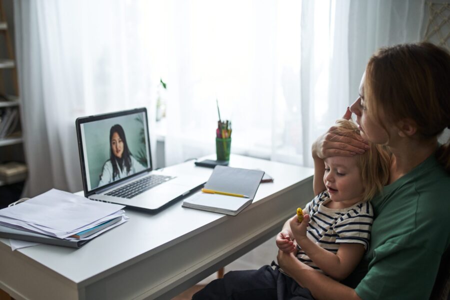 A young mother with a sick child consults a laptop with a doctor online from home. Health and treatment of children at home online. Telemedicine
