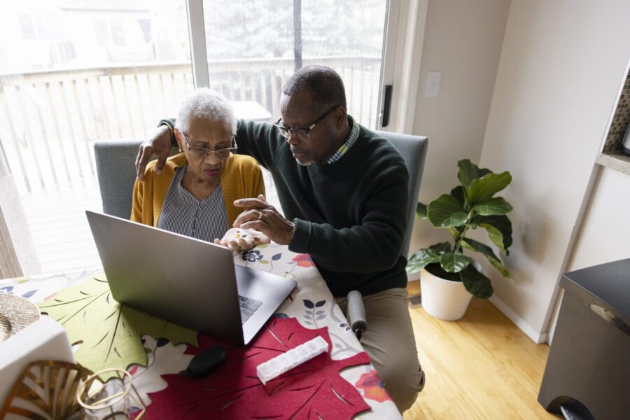Senior couple with medication video chatting in telemedicine appointment at laptop in dining room