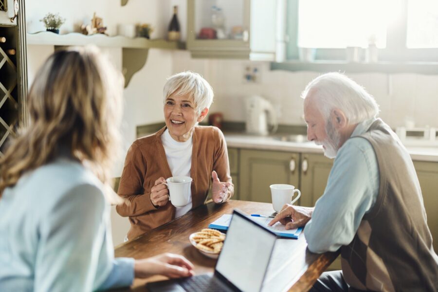 Happy senior woman talking to insurance agent during a meeting at home while her husband is going through contract.