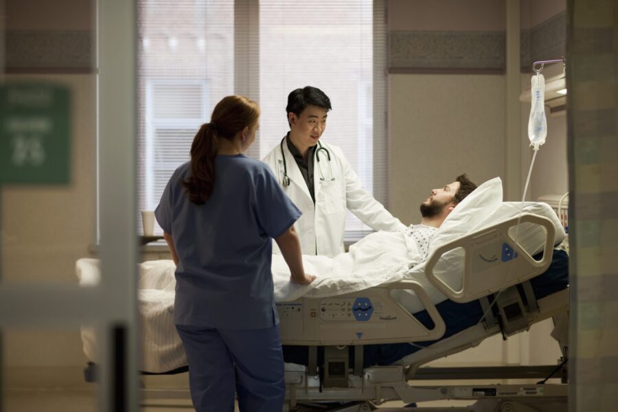 20s male patient in hospital bed listening to doctor and nurse in hospital