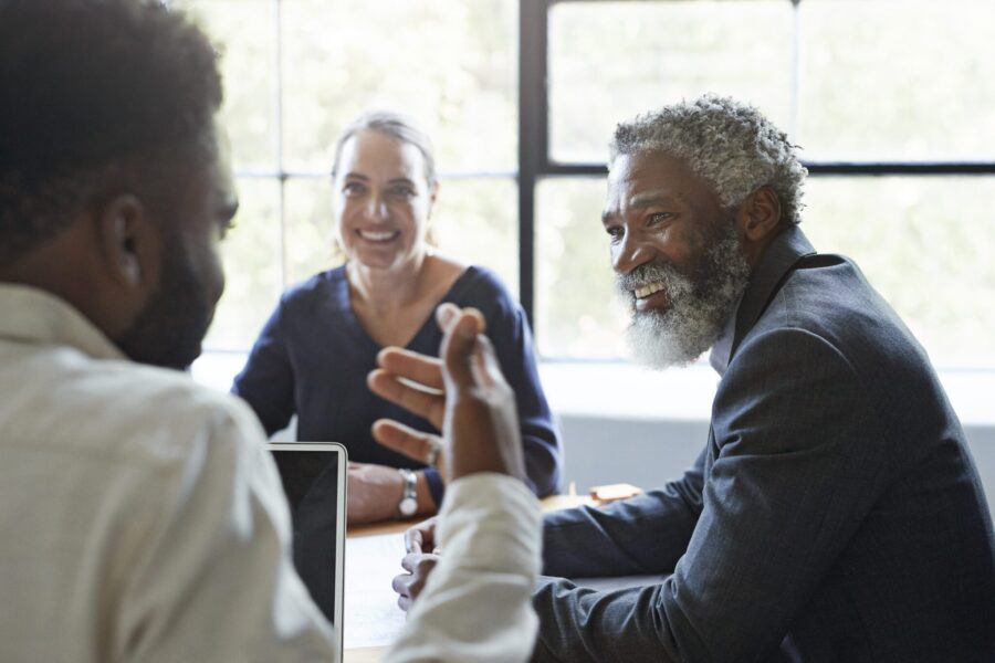 Smiling businessman looking at male coworker while sitting in board room during office meeting