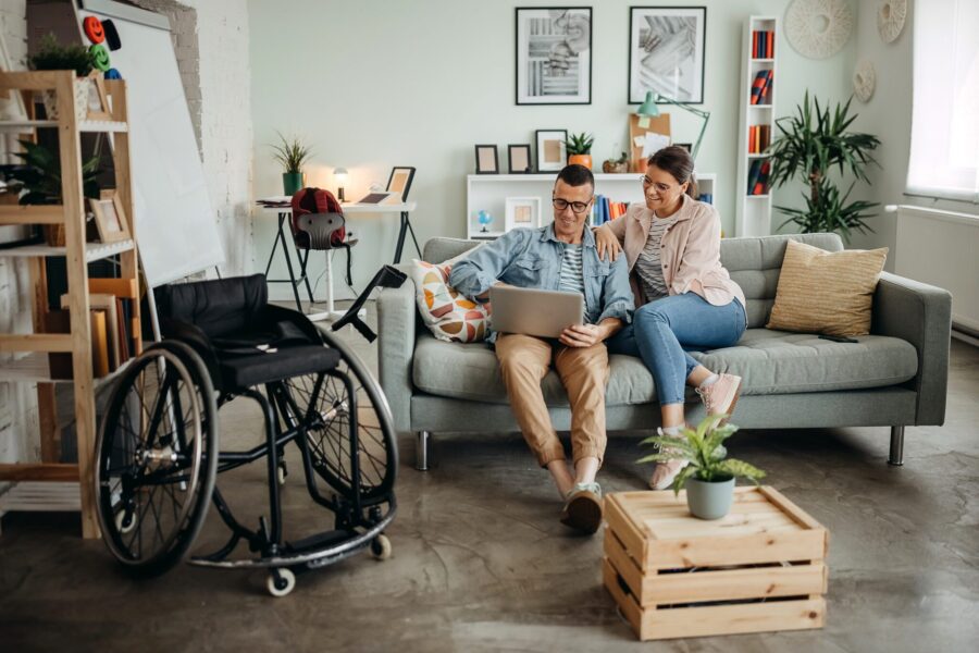 Disabled man and his wife are sitting on the bed and using a laptop