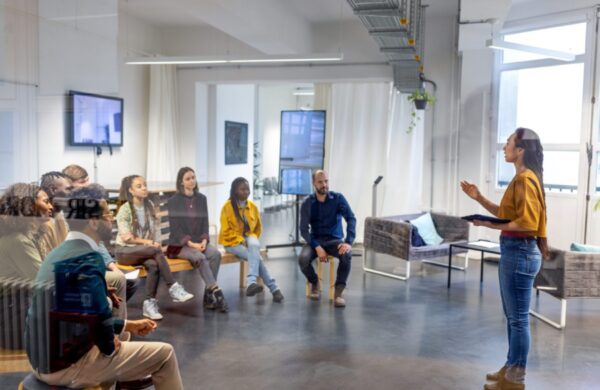 Young asian businesswoman speaking to her coworkers in meeting. Female addressing colleagues sitting in front inside office.