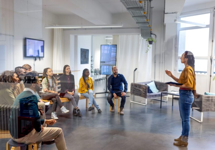 Young asian businesswoman speaking to her coworkers in meeting. Female addressing colleagues sitting in front inside office.