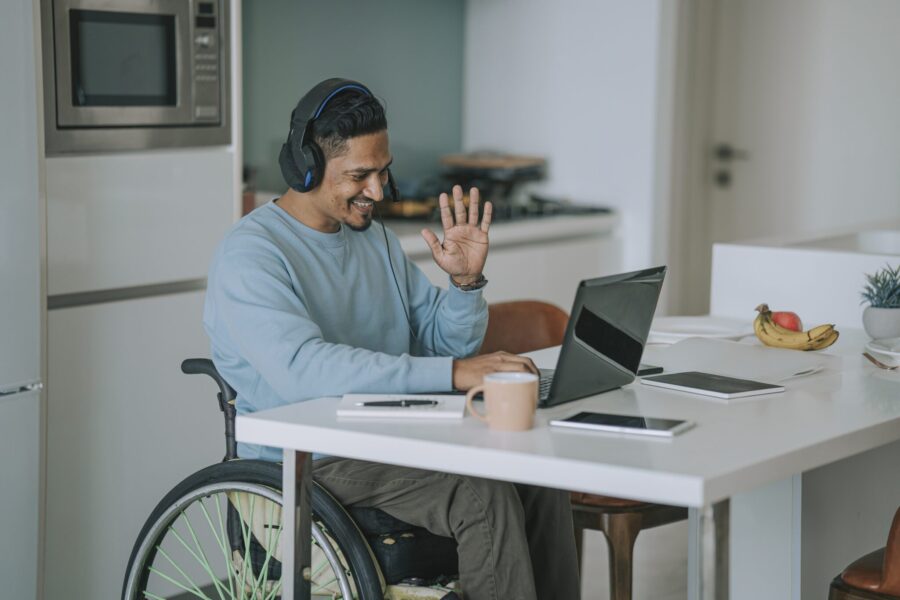 Asia Indian with disability sitting on wheelchair in dinning room video call with laptop