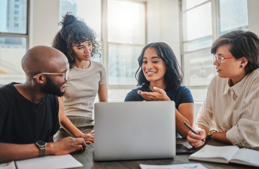 Laptop, digital marketing and team in a meeting planning seo, advertising and innovation strategy as a group. Creative, diversity and young people working on branding ideas for a startup project