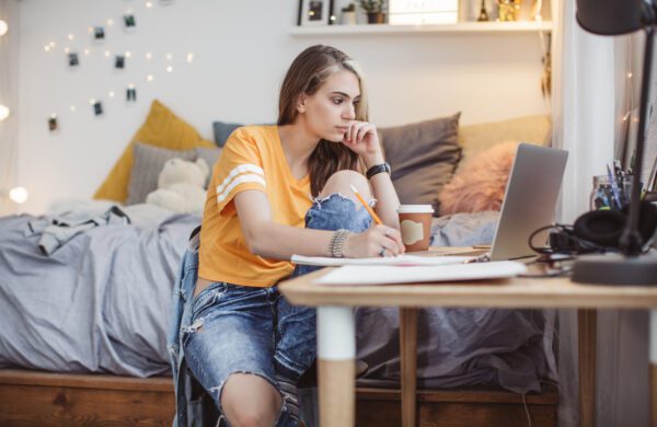 Young woman alone in bedroom. She is working homework and using laptop