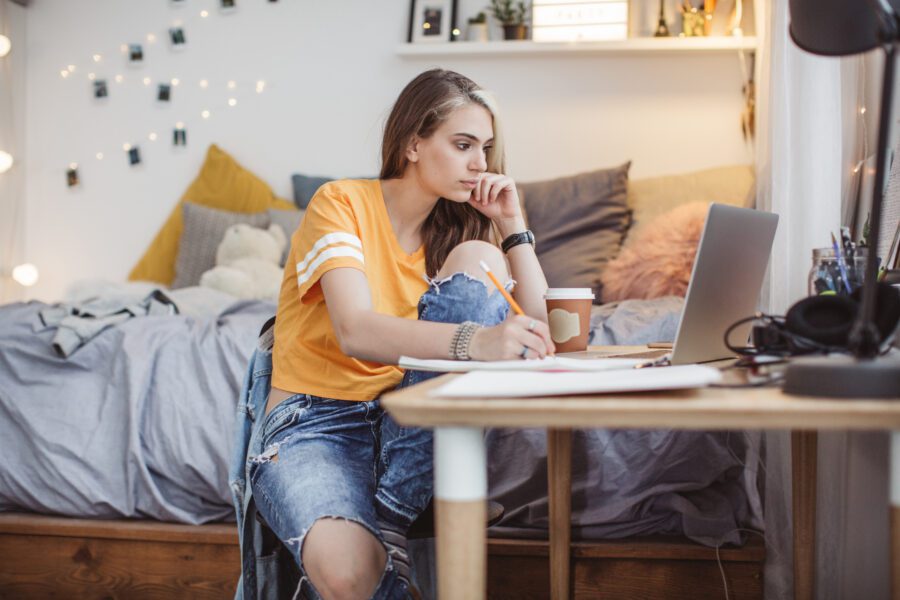 Young woman alone in bedroom. She is working homework and using laptop