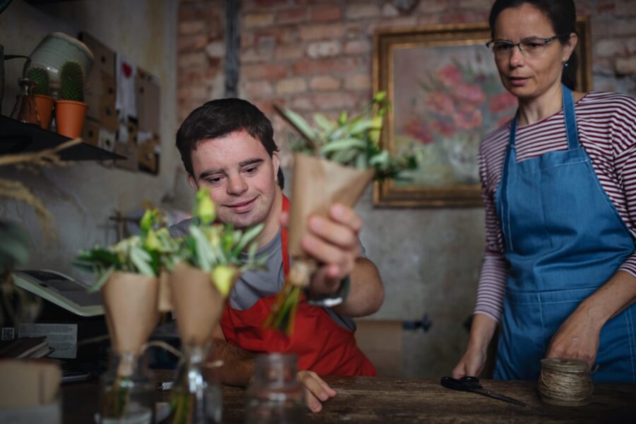 Happy, confident florist with special needs working with his colleague in flower shop