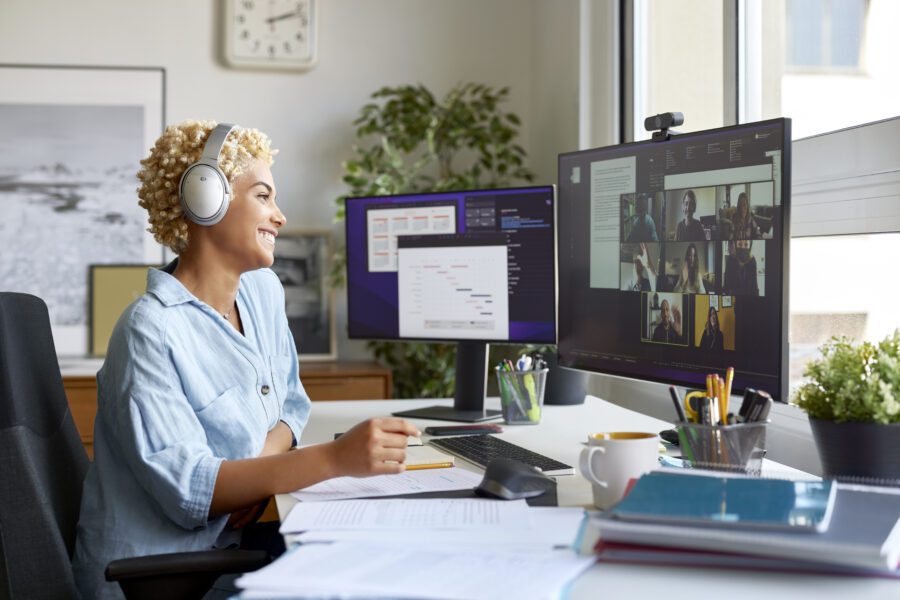 Cheerful businesswoman holding document during video conference with colleagues. Smiling blond Afro female professional is working at home office. She is wearing wireless headphones.