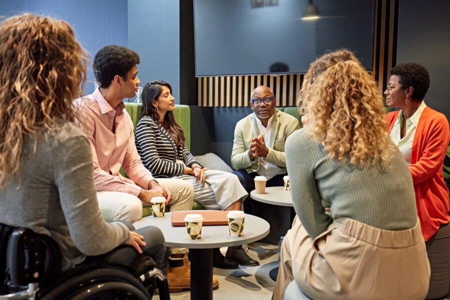 Multiracial male project manager in late 50s talking with diverse team enjoying coffee and update on planning and development.