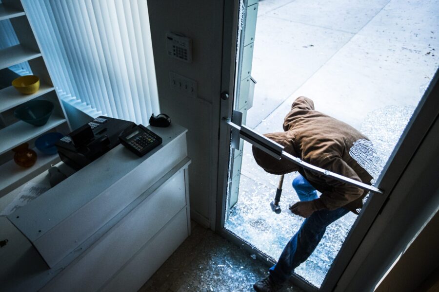 A robber using a sledgehammer to break the glass of a retail store.