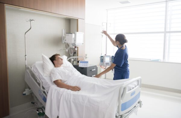 Young man in hospital being cared for by nurse. Medical professional looking after patient on hospital ward. Adjusting iv line, medication, care, bedside manner.