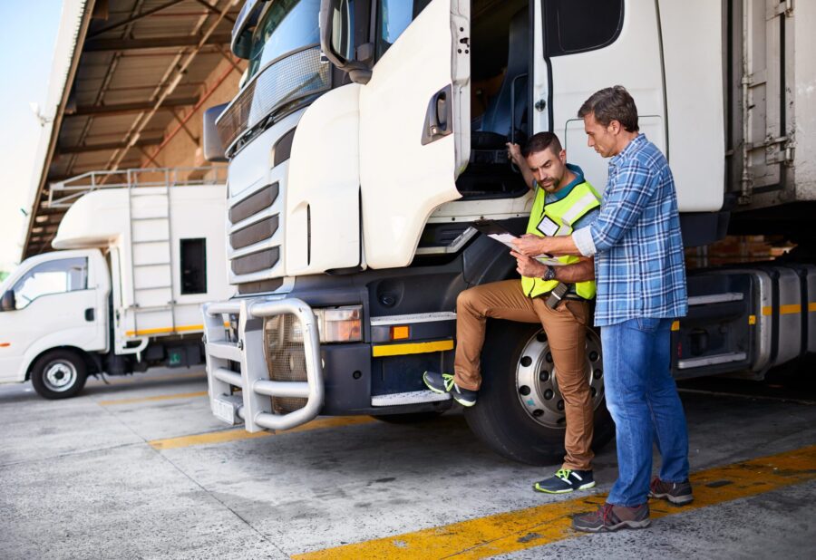 Shot of two coworkers talking together next to a large truck outside of a distribution center