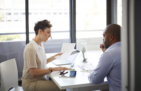 Coworkers having discussion holding papers, tablet, laptop and phone on the table