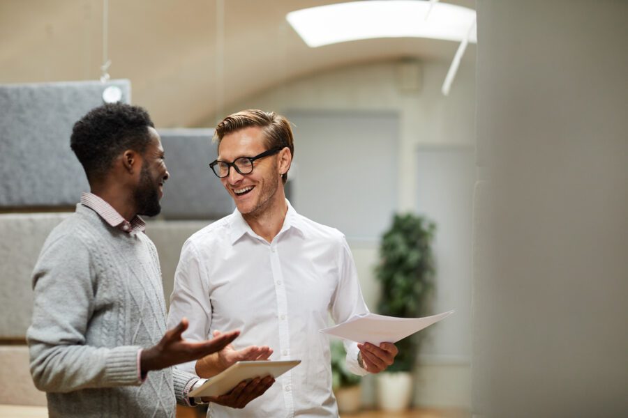 Cheerful Excited Young Colleagues Standing In Modern Office And Shrugging Shoulders While Coming To Common Decision