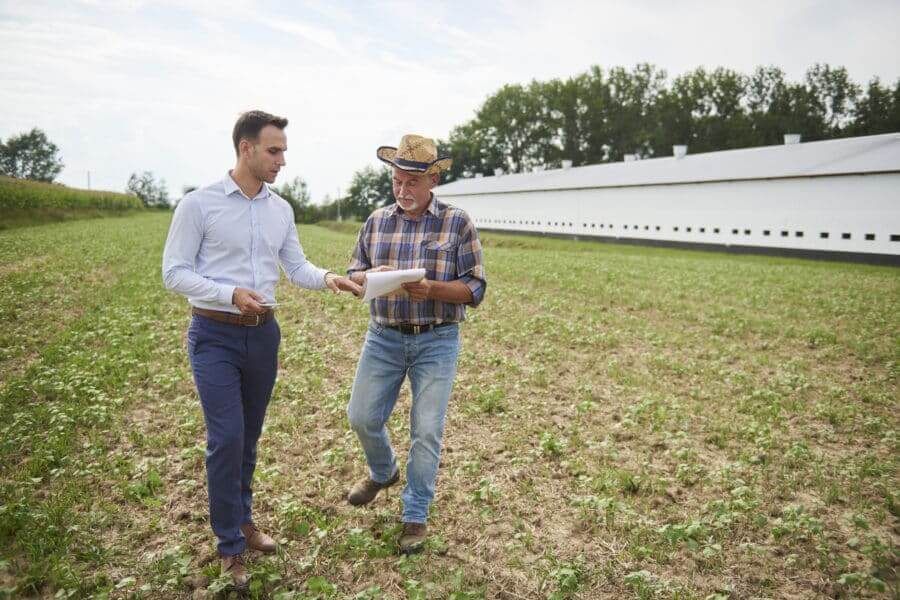 Farmer And Businessman Discussing Data From Clipboard On The Field