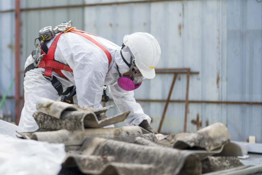 Workers wearing protective clothing while removing the asbestos roof. Hazardous waste management and working safety concept. Professional waste disposal.