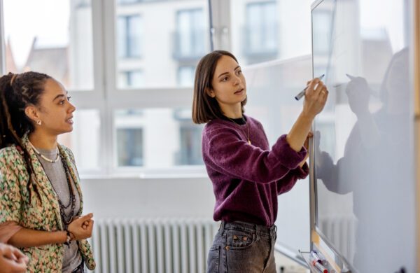 Businesswoman brainstorming ideas on whiteboard with colleague. Female business partners having brainstorming session in startup meeting room.