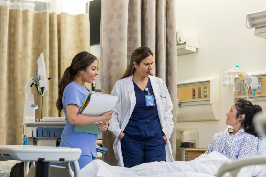 The female doctor and nurse stand bedside mid adult woman patient