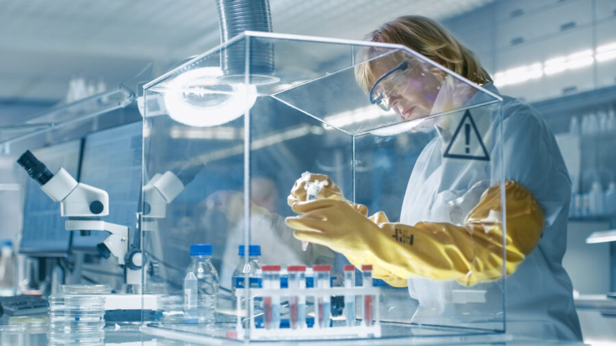 Senior Female Epidemiologist Works with Samples in Isolation Glove Box. She's in a Modern, Busy Laboratory Equipped with State of the Art Technology.