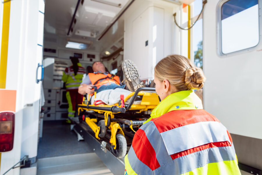 Paramedics in uniform putting injured man on stretcher in ambulance car