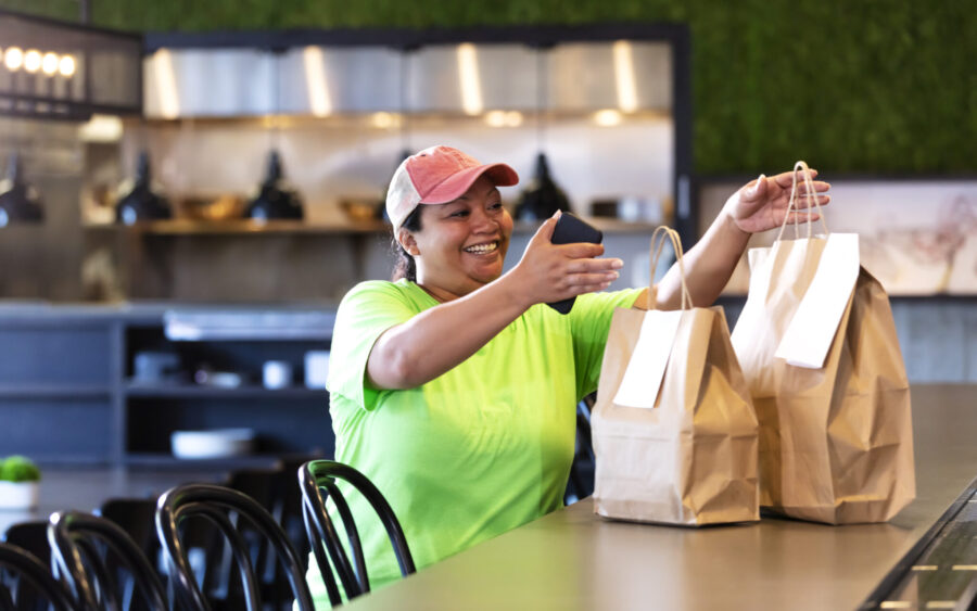 A delivery person smiling as she picks up a takeout food order off the counter