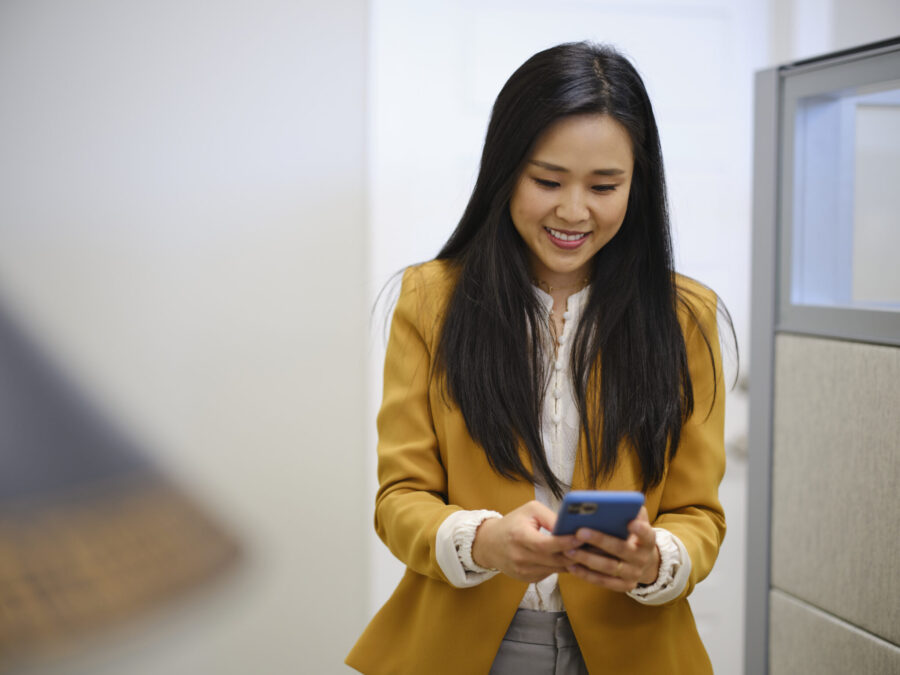 A Korean woman in an office, sending and receiving text messages on a smartphone.