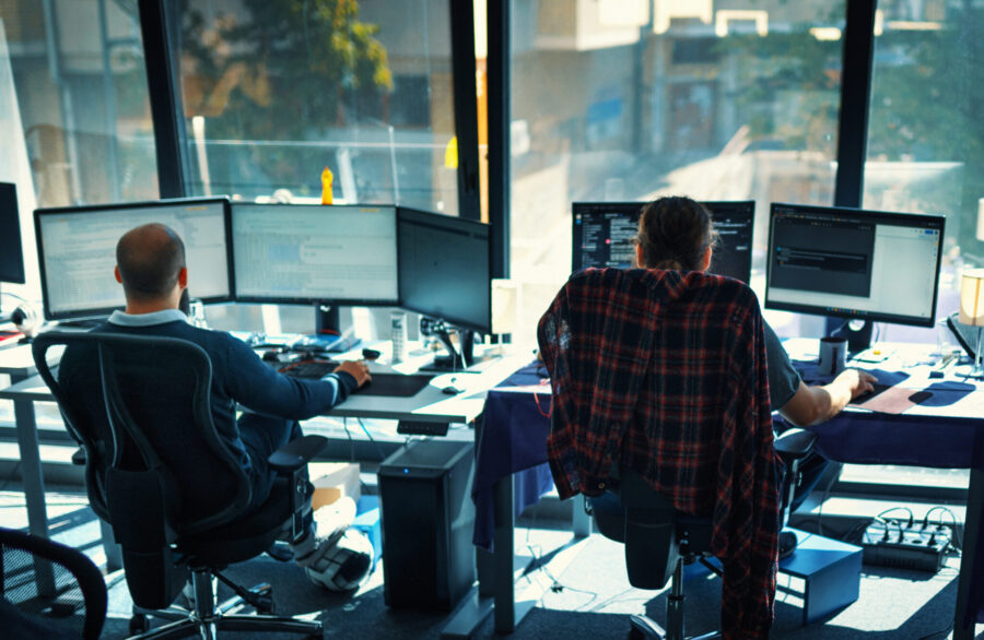 Closeup rear view of a young man coding on multiple computers