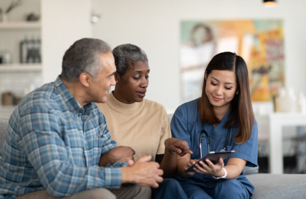 A young doctor of Asian descent and an elderly couple look at her tablet as she shares the results of their at home check-up.