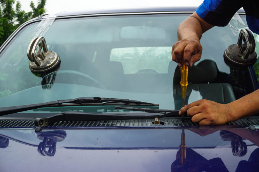 Glazier using tools repairing to fix crack broken windshield on the front window glass of the machine car accident.