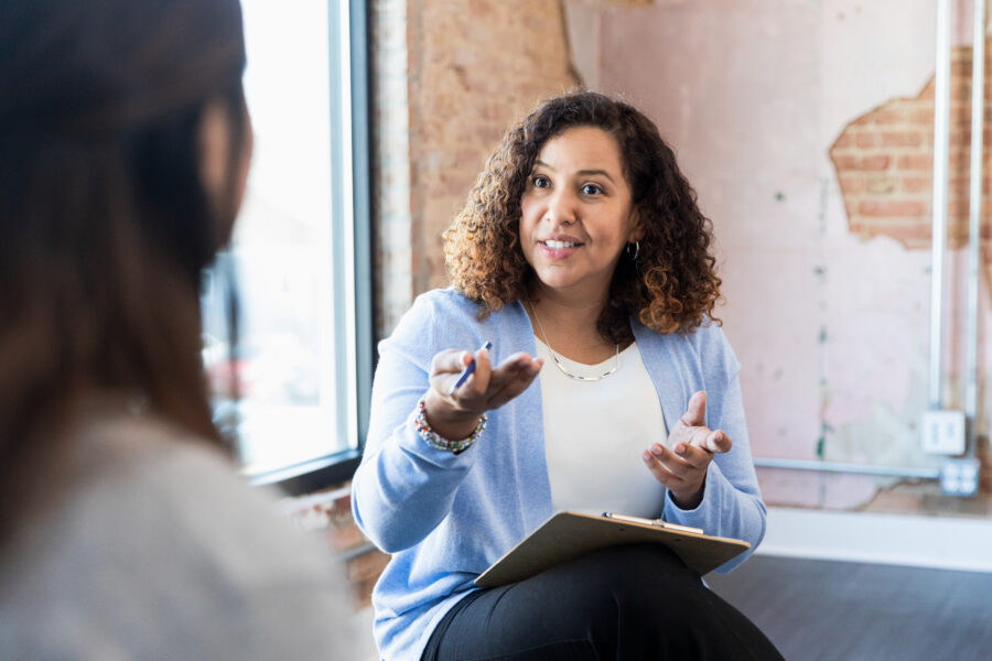 Meeting one-on-one, female therapist gestures toward unrecognizable woman